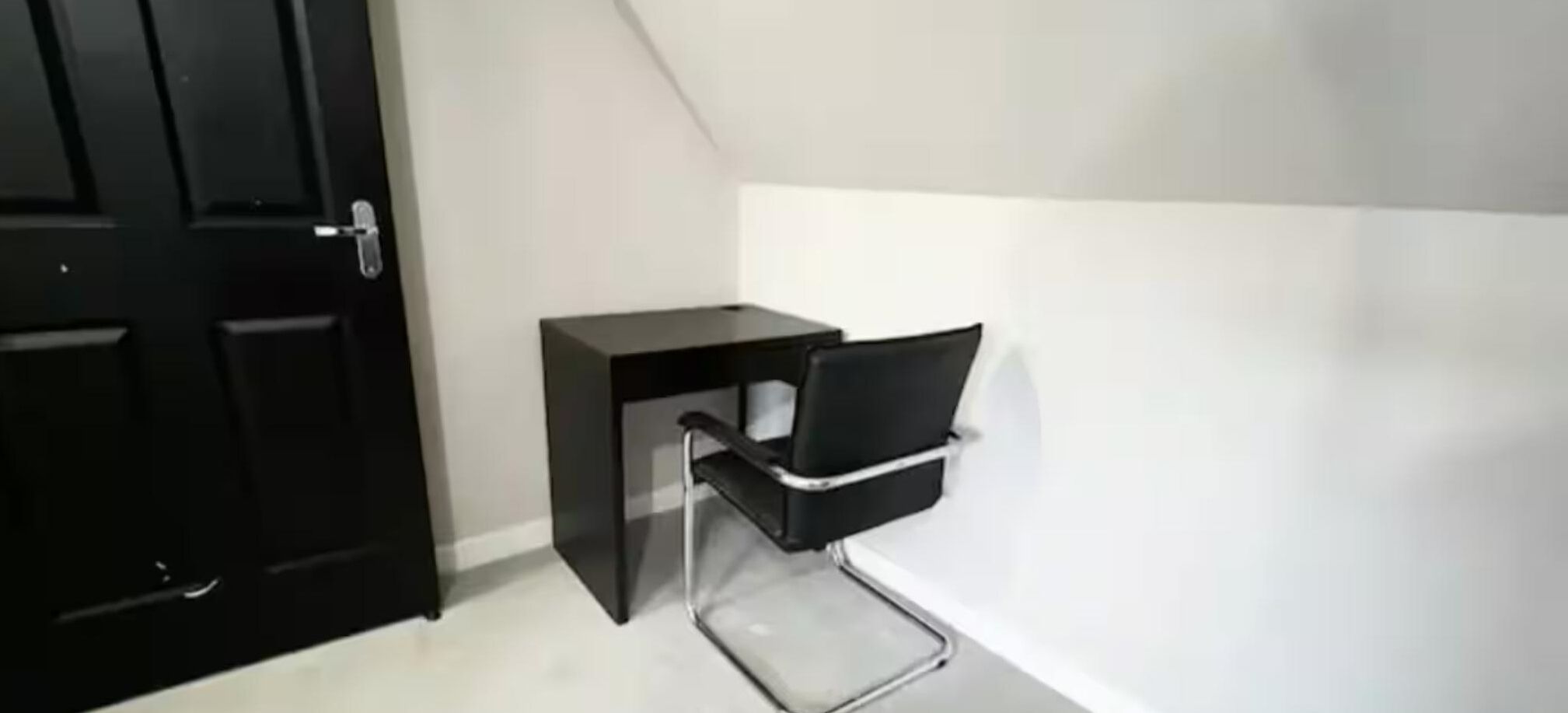 A corner room with a black door, a small black desk, and a white wall.