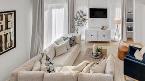 Ett modernt vardagsrum med en hörnsoffa, en vit TV-möbel och en golvlampa.