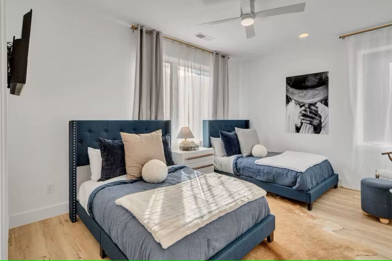 Une chambre moderne avec deux lits, un ventilateur de plafond, une télévision et une grande fenêtre avec des rideaux.