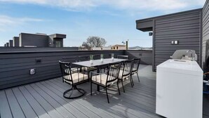 En takterrass med ett bord och stolar, en grill och utsikt över staden.