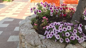 Área externa com assentos laranja, guarda-sóis, um vaso de pedra com flores e vista para o mar.