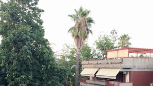 Um edifício de vários andares com telhado vermelho e toldos brancos, cercado por vegetação exuberante e árvores.