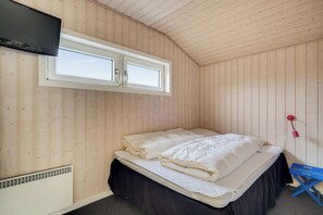 A wooden-paneled room with a bed, a TV mounted above a window, and a heater. - Bjålumvej 17 (Norre Nebel)