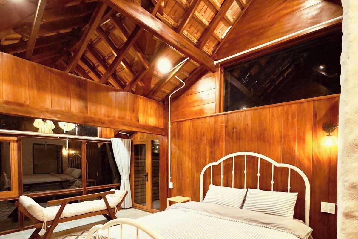 Una stanza in legno con un letto, una panca e un'ampia finestra.