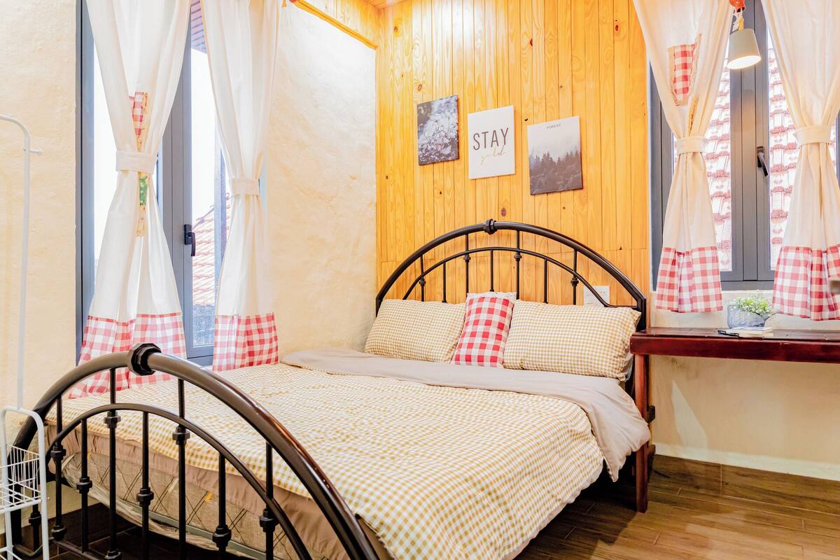 Una camera accogliente con una parete in legno, un letto con biancheria a quadretti e una finestra con tende.