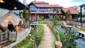 A two-story building with a red roof, a wooden deck, and a small pond. - The Monhi Da Lat (Xuan Huong - Da Lat)