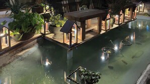 An indoor pool area with a wooden table and chairs, surrounded by potted plants and illuminated by string lights. - The Monhi Da Lat (Xuan Huong - Da Lat)