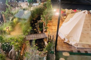 Un área con carpas y una terraza de madera, rodeada de vegetación exuberante y un arroyo pequeño.