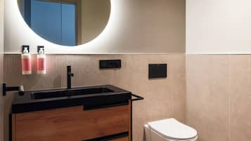 Een moderne badkamer met een ronde spiegel, een zwarte wastafel, een houten meubel en een wit toilet.