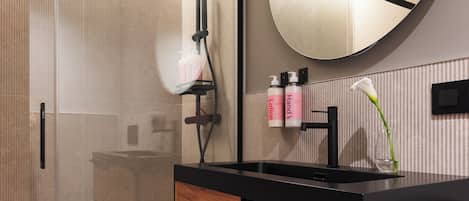 A modern bathroom with a glass shower enclosure, a wooden vanity with a black countertop, and a round mirror.