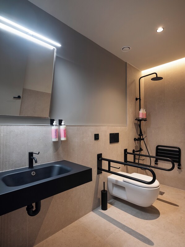 Un baño moderno con un lavamanos negro, un inodoro blanco, un cabezal de ducha de mano y un perchero para toallas.