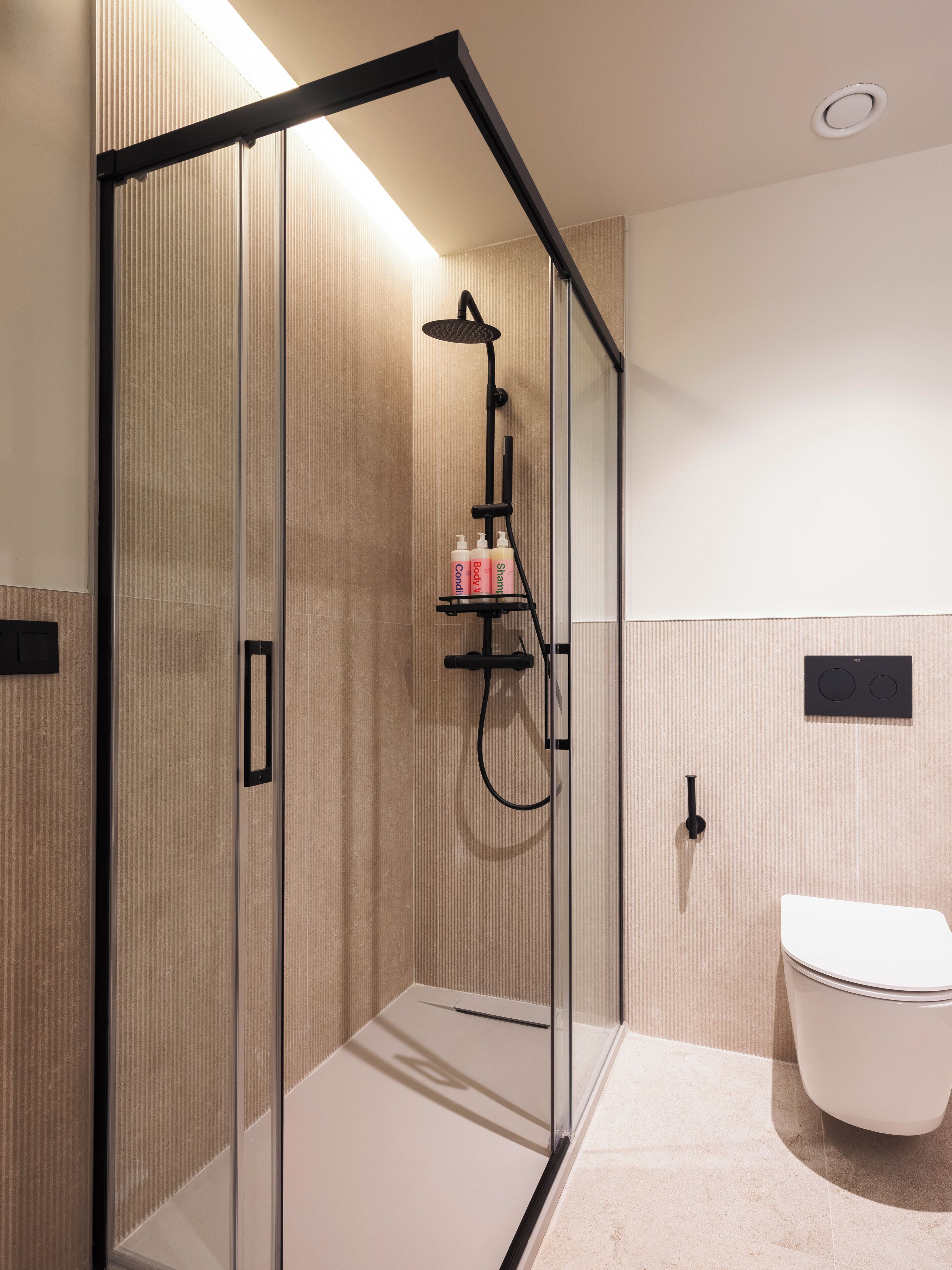 A modern bathroom with a glass-enclosed shower, a white toilet, and a towel rack with toiletries.