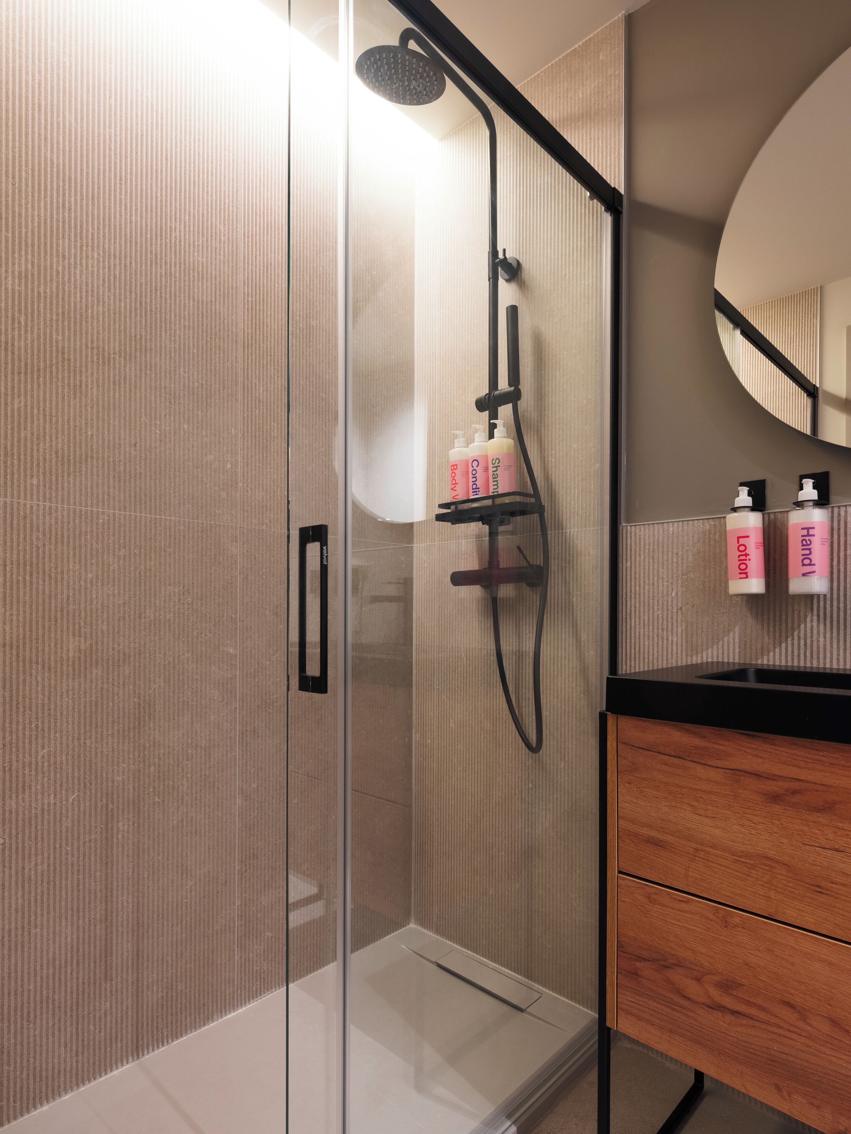 Un bagno moderno con cabina doccia in vetro, mobile bagno in legno e uno specchio.