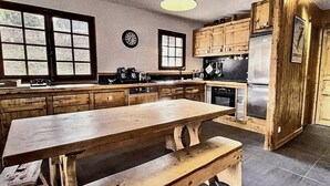 Une cuisine avec des meubles de rangement en bois, une grande table en bois et un luminaire suspendu.