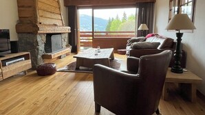 Un salon chaleureux avec une cheminée en pierre, des meubles en bois et un balcon offrant une vue sur les montagnes.