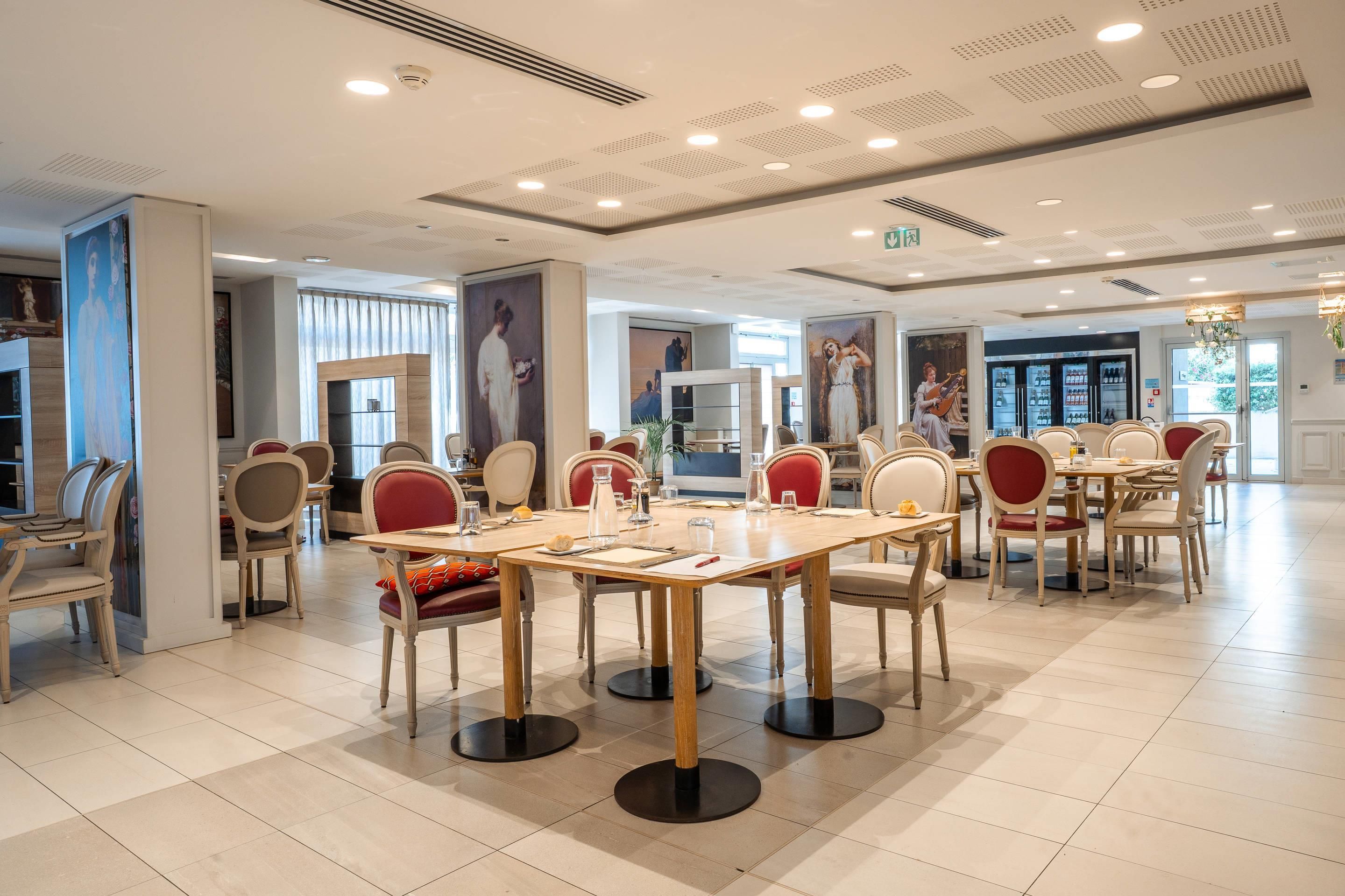 A spacious dining area with multiple tables and chairs, featuring a modern ceiling design and large windows.
