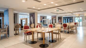A spacious dining area with multiple tables and chairs, featuring a modern ceiling design and large windows.
