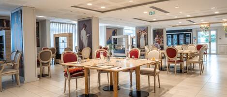 A spacious dining area with multiple tables and chairs, featuring a modern ceiling design and large windows.