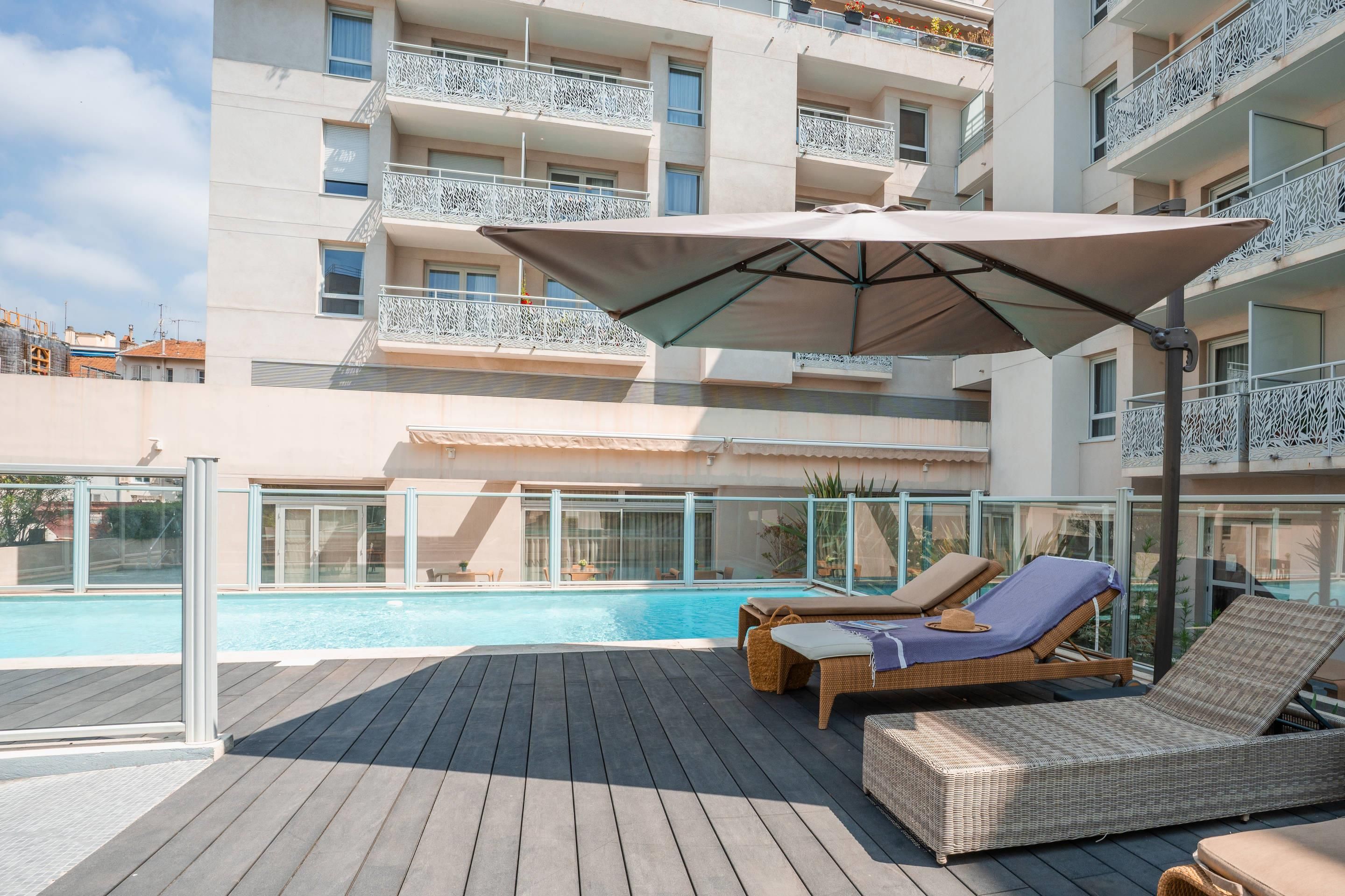 A rooftop pool area with lounge chairs and a large umbrella.