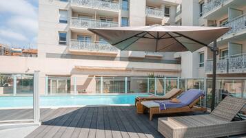 A rooftop pool area with lounge chairs and a large umbrella.