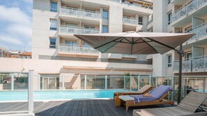 Un espace piscine aménagé sur le toit, avec des chaises longues et un grand parasol.