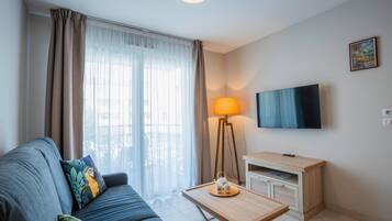 Een moderne woonkamer met een bank, een salontafel, een lamp, een televisie en een klein kastje.