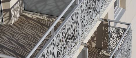 Un balcon extérieur à plusieurs niveaux, doté de garde-corps en métal aux motifs complexes et d’un plancher en bois.