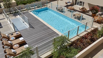 A rooftop swimming pool with sun loungers and a glass railing.