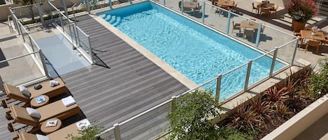 Une piscine sur le toit, dotée de chaises longues et d’une rambarde en verre.