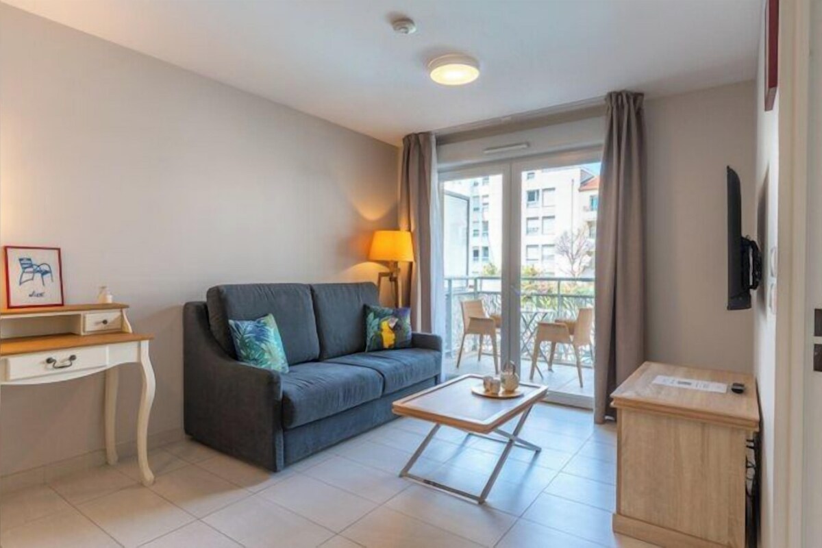 A living room with a sofa, a desk, a lamp, and a balcony with chairs.