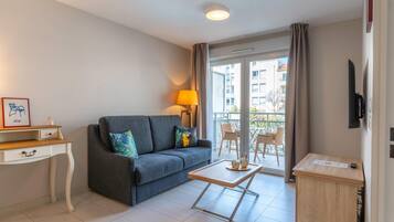 En moderne stue med sofa, et lille bord, en lampe og udsigt til den tilstødende balkon.