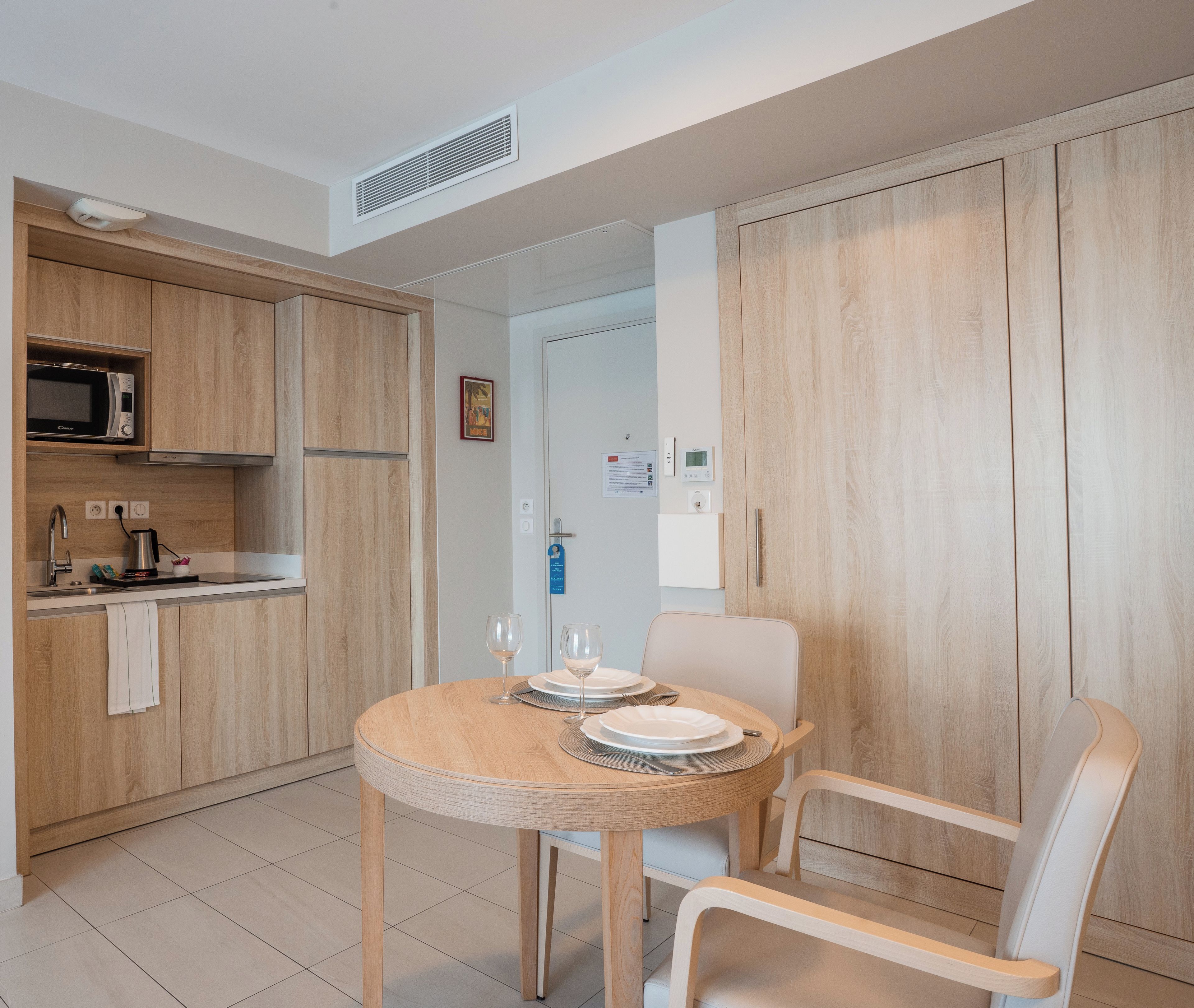 A modern kitchen with wooden cabinets, a microwave, and a sink. There is a dining table with chairs and a small rug.