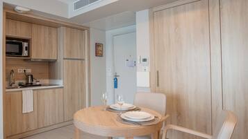 A modern kitchen with wooden cabinets, a microwave, and a sink. There is a dining table with chairs and a small rug.