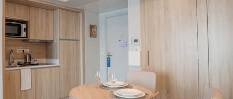 A modern kitchen with wooden cabinets, a microwave, and a sink. There is a dining table with chairs and a small rug.