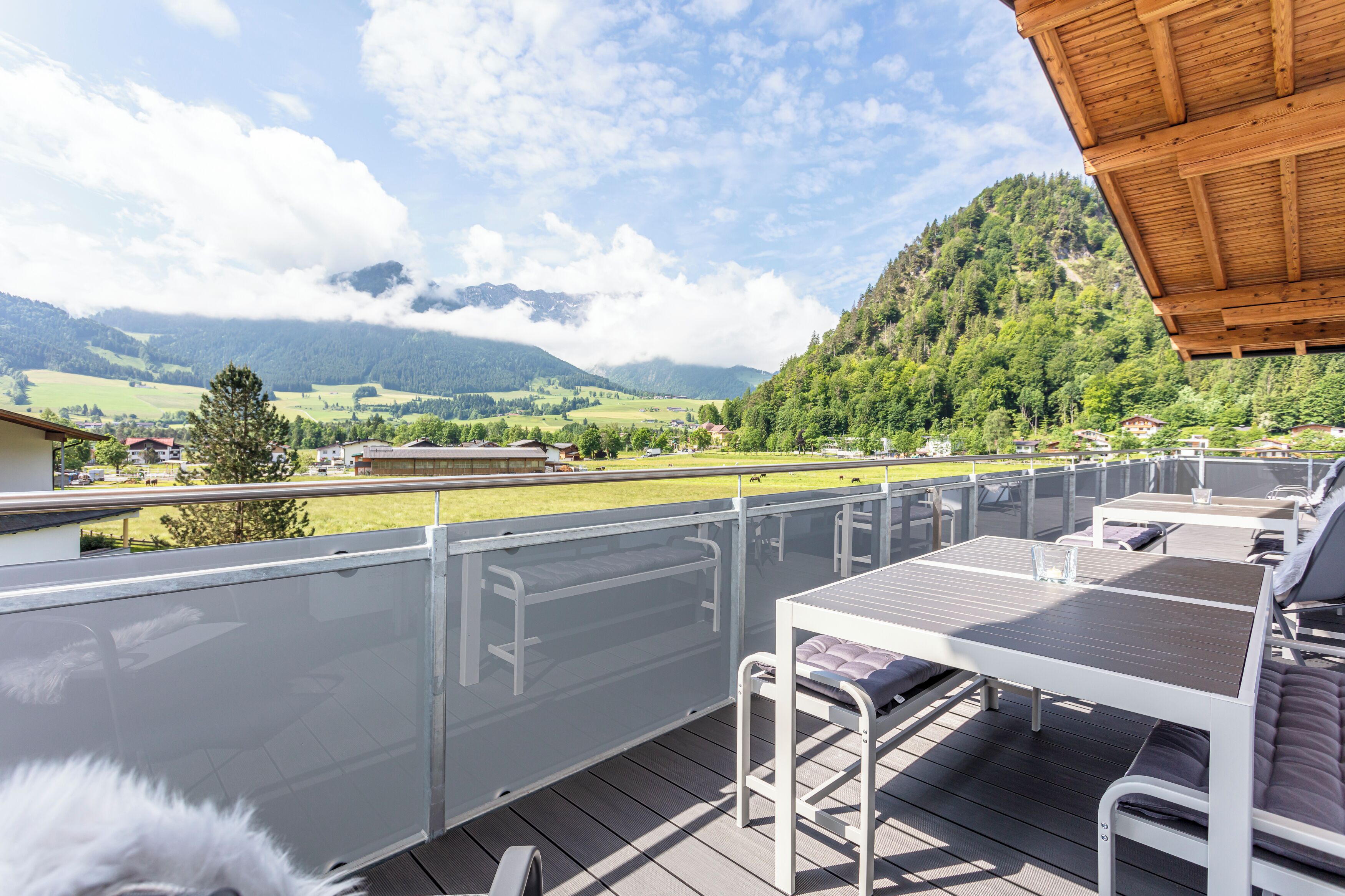 A deck with a table and chairs, overlooking a mountainous landscape.