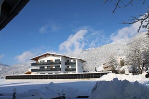 En modern, flervåningsbyggnad med balkonger, omgiven av snötäckta berg och träd.