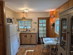 Una cocina funcional con refrigerador, microondas, lavamanos y armarios de madera.