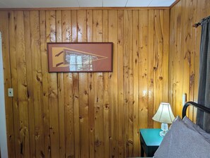 Una habitación con paneles de madera, un cuadro enmarco, una lámpara y una cama.