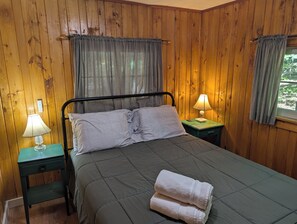 Una habitación con paneles de madera, una cama, dos lámparas de noche y un ventanal con cortinas.