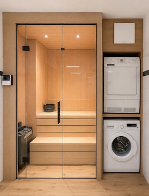 Een kleine wasruimte met een ingebouwde wasmachine en droger, houten kastjes en een zithoekje.