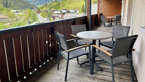 A wooden deck with a round table and chairs, overlooking a mountainous landscape.