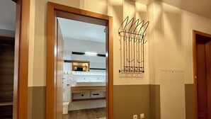 A hallway with a wooden floor, a white wall with a metal rack, and a door leading to a bathroom.