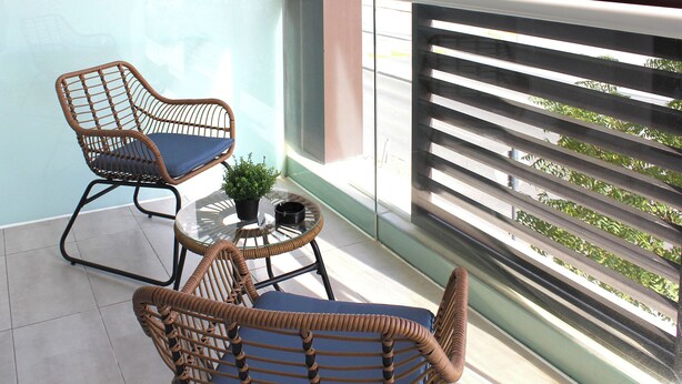 A balcony with wicker furniture, a small table with a plant, and a view of the street. - Bloomfields STU with Balcony Leonardo (Abu Dhabi)