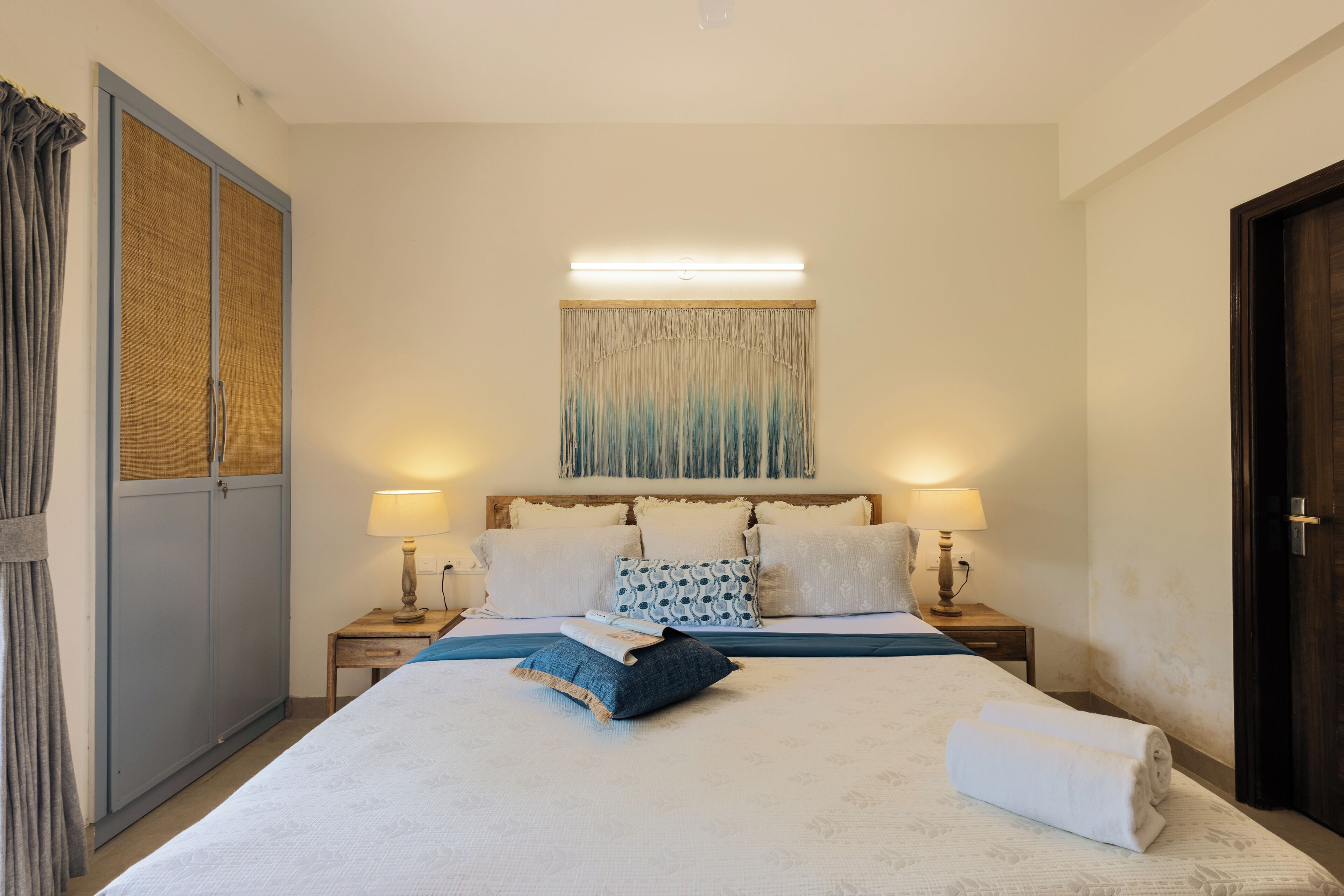 A neatly arranged hotel room with a large bed, two bedside tables with lamps, a headboard with curtains, and a door on the right.