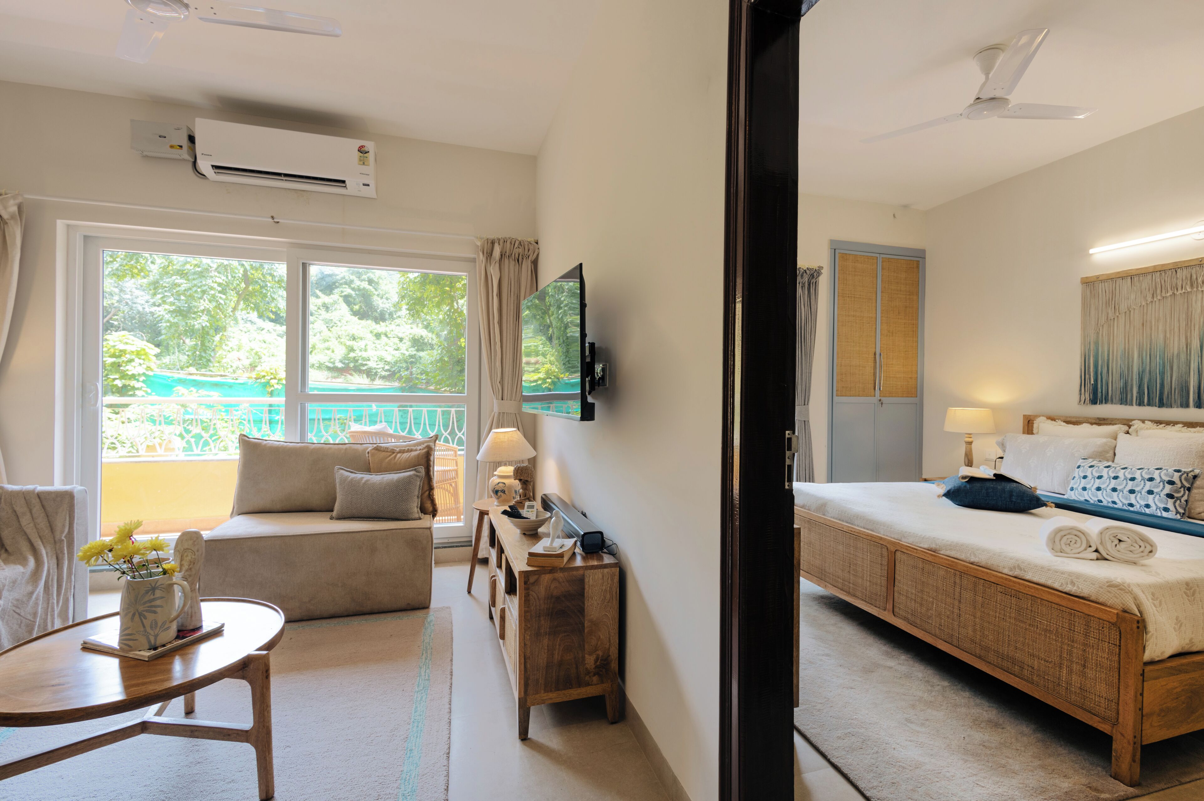 Una habitación de hotel con cama, sofá, una mesita de noche con lámpara, televisor montado en la pared y aire acondicionado.
