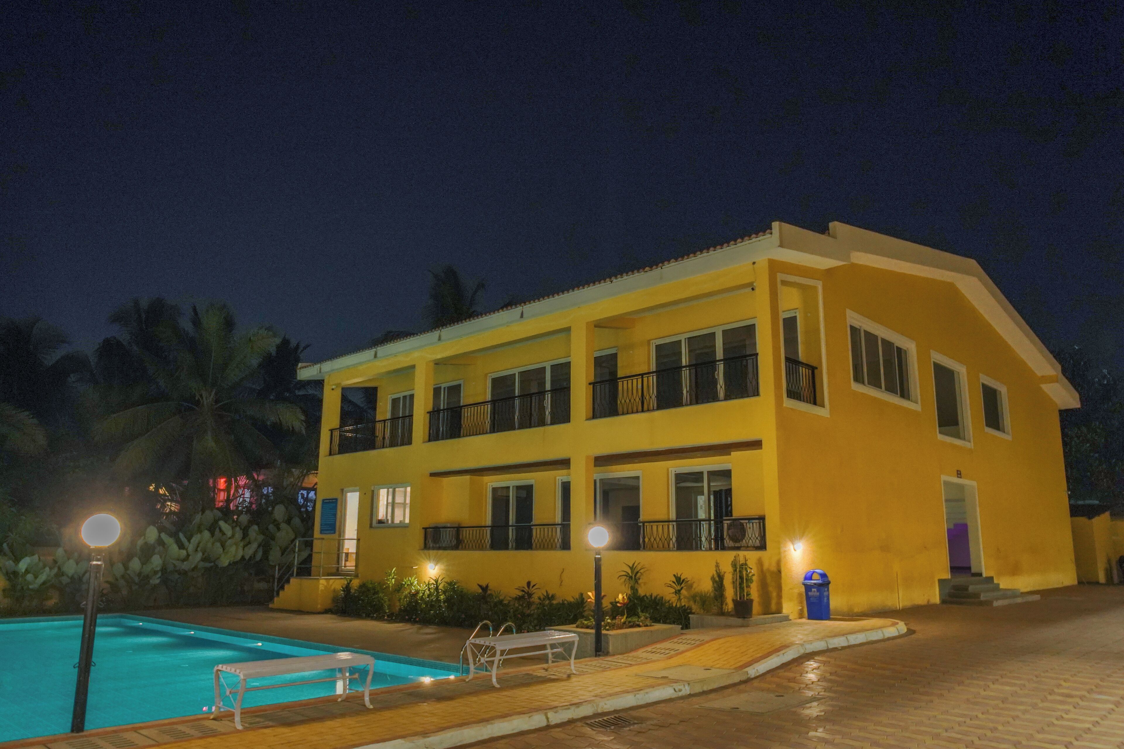 A two-story building with a swimming pool, outdoor seating, and a well-lit entrance.