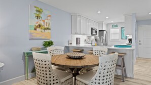 Een moderne keuken met witte kastjes, een houten eettafel en rieten stoelen.