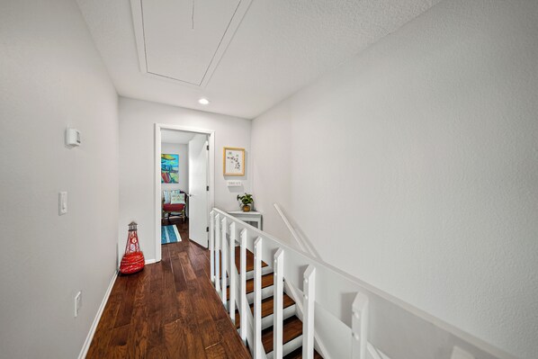 A hallway with a wooden floor, white walls, and a white railing.
