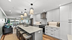 A modern kitchen with a central island, bar stools, and a dining area with a view. - Bayfront Boca Grande North 43 - Top Floor - 2/2 Great Water Views! (Placida)