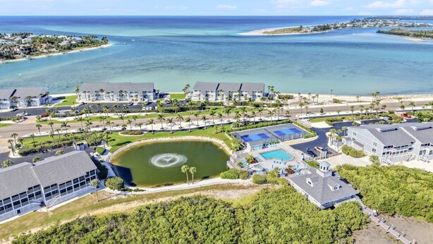 An aerial view of a coastal resort with multiple buildings, a central pool, and a large body of water. - Bayfront Boca Grande North 43 - Top Floor - 2/2 Great Water Views! (Placida)